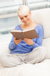 Smiling woman relaxing while reading a book on the sofa