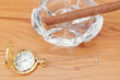 Retro image of gold pocket watch and a Havana cigar in the ashtr