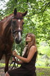 Young girl sitting on the bench and chestnut horse standing near