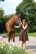 Beautiful girl in dress and horse portrait near the flower bed