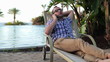 Young man on sunbed by the pool talking on cellphone