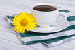 A cup of coffee and chamomile on a wooden table with a napkin