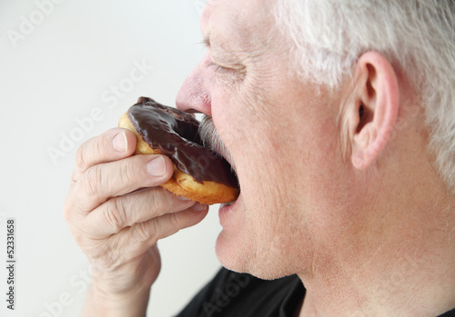 Photo: man takes bite of chocolate glazed doughnut man takes bite of chocolate glazed doughnut