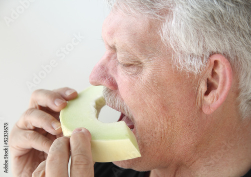 Photo: senior man eats fresh honeydew melon senior man eats fresh honeydew melon