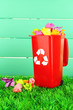 Recycling bin with papers on grass on light blue background