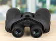 Black modern binoculars on wooden table on window background