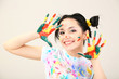 Young pretty painter with hands in paint, on gray background