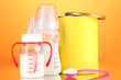 Bottles with milk and food for babies on orange background