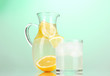 Lemonade in pitcher and glass on green background