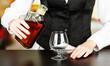 Barman hand with bottle of cognac  pouring drink into glass,