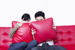Asian couple hide behind pillow on red sofa - isolated