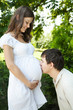 Husband kissing his pregnant wife belly outdoors