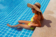 Young woman in a yellow swimsuit seating down in a swimming pool