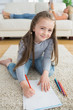 Happy girl drawing with her mother reading newspaper