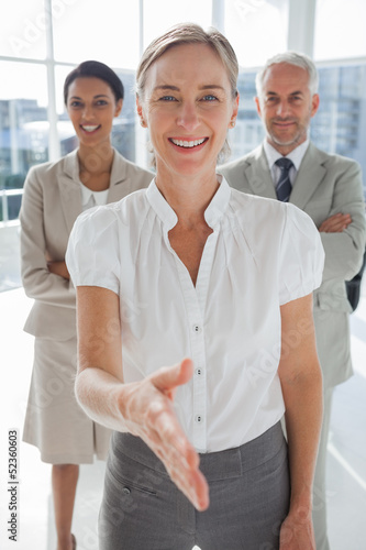 Photo: Smiling businesswoman giving a handshake with colleagues behind Smiling businesswoman giving a handshake with colleagues behind