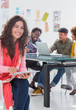 Smiling woman  using tablet with creative team working behind