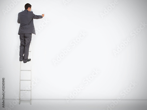 Photo: Businessman standing on ladder drawing on large copy space Businessman standing on ladder drawing on large copy space