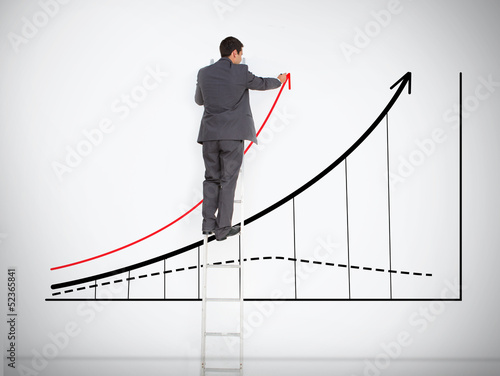 Photo: Businessman standing on ladder drawing large graph Businessman standing on ladder drawing large graph
