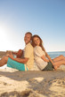 Young couple sat back to back on the beach