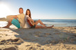 Happy couple sat back to back on the beach 