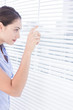 Attractive businesswoman peeking through venetian blind