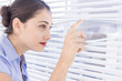 Pretty businesswoman peeking through a venetian blind