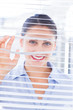 Cheerful businesswoman smiling through venetian blind