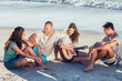 Friends sitting on the sand playing guitar