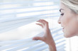 Blonde woman peeking through venetian blinds