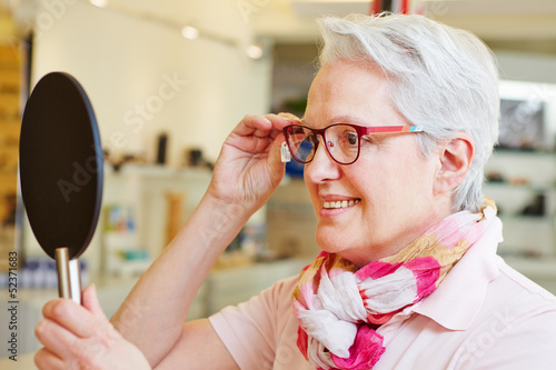 Photo: Seniorin mit Brille schaut in Spiegel Seniorin mit Brille schaut in Spiegel