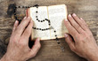 Hands holding the Bible and praying with a rosary