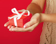 Photo: Female hand holding gift box isolated on red background Female hand holding gift box isolated on red background