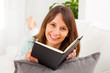 Young woman stretching comfortably on couch and reading a book