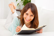 Young woman stretching comfortably on couch and reading a book