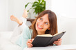 Young woman stretching comfortably on couch and reading a book