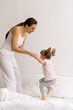 A little girl jumps on the bed with her mom