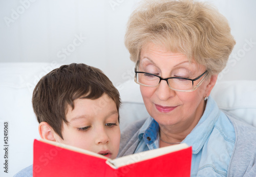 Photo: Grandmother and little boy reading book happy together at home Grandmother and little boy reading book happy together at home