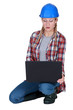 Young female builder crouching with laptop