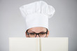 Woman in chef's hat looking at camera over the cookbook