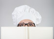 Photo: Woman in chef's hat looking over the cookbook, grey background Woman in chef's hat looking over the cookbook, grey background