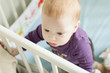 Top view of adorable baby boy trying to stand up in his cot