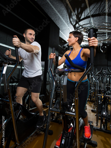 Photo: elliptical walker trainer man and woman at black gym elliptical walker trainer man and woman at black gym