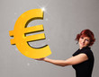 Foto: Beautiful girl holding a big 3d gold euro sign Beautiful girl holding a big 3d gold euro sign