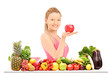 Female holding an apple and posing behind a table full of vegate