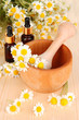 Essential oil and chamomile flowers in mortar on wooden table
