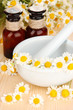 Essential oil and chamomile flowers in mortar on wooden table