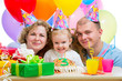 kid girl with parents blow candles on birthday cake