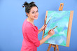 Beautiful young woman painter at work, on color background
