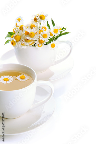 Photo: Cups of herbal tea and wild camomiles, isolated on white Cups of herbal tea and wild camomiles, isolated on white