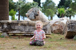 Little blonde smiling girl sits among ancient ruins, Pamukkale,